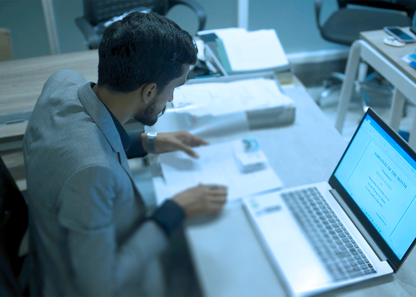 South Asian male sitting at his work desk with his laptop open.